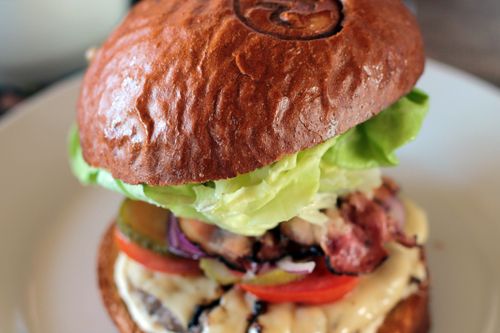 Free Close-up of a gourmet hamburger with fresh lettuce, cheese, and bacon on a plate. Stock Photo