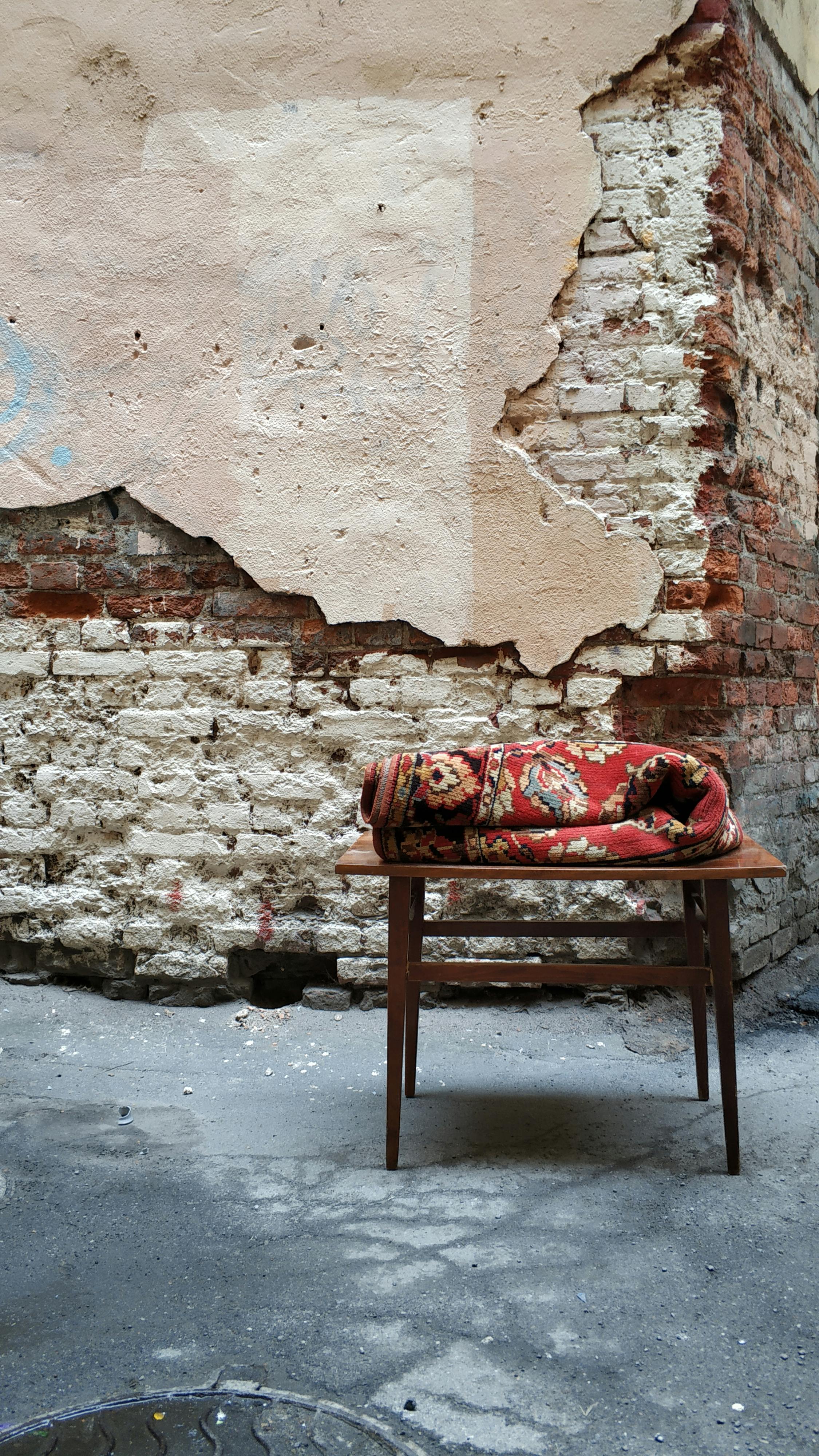 Rustic scene of a brick wall with a vintage wooden table and rolled carpet.