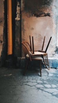 Rustic wooden chairs in an abandoned room with worn walls and vintage charm.