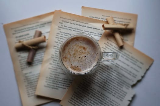 A warm cup of coffee surrounded by old books and cinnamon sticks on a rustic tabletop.