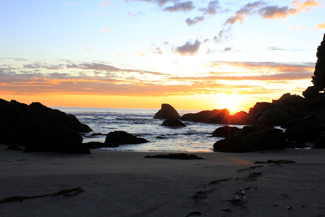 オレンジ色の夕日の下のビーチと岩