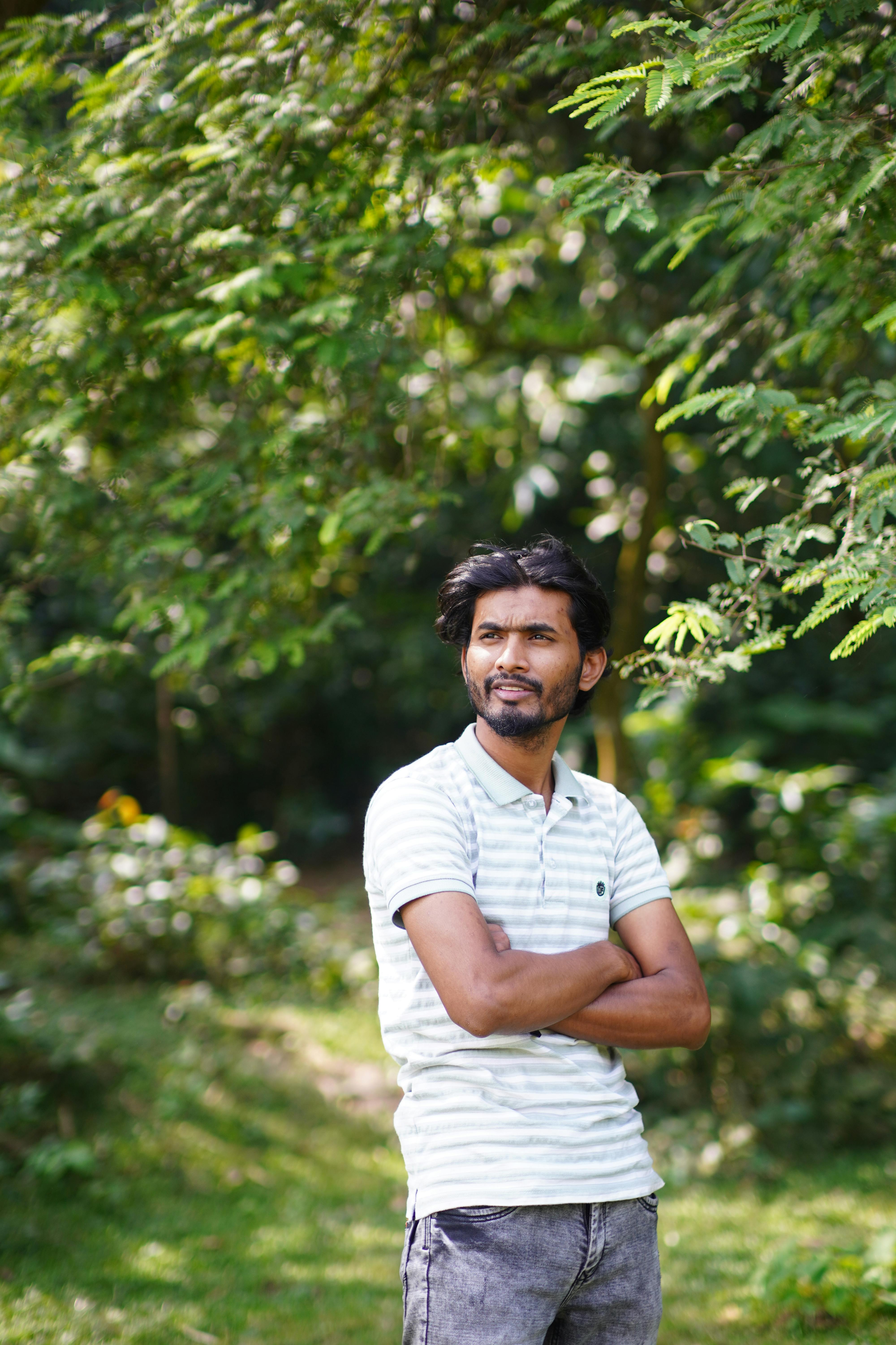 A man in casual attire stands confidently amidst lush greenery, enjoying a sunny day outdoors.