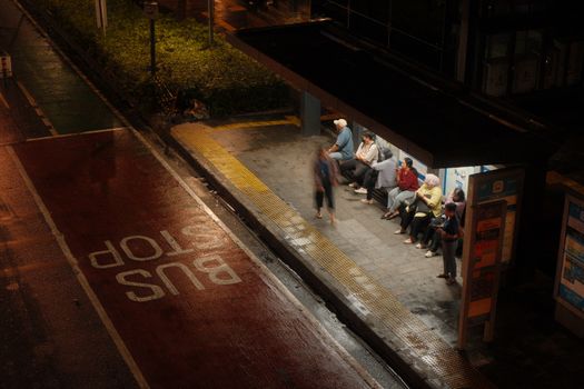 A dimly lit bus stop at night with diverse passengers waiting under shelter.