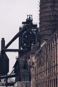 Wide angle view of an old industrial factory with prominent pipes and chimney on a cloudy day.