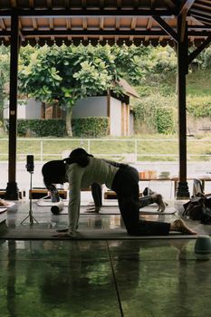 Adults practicing yoga poses at an open-air pavilion in Jawa Barat, Indonesia.