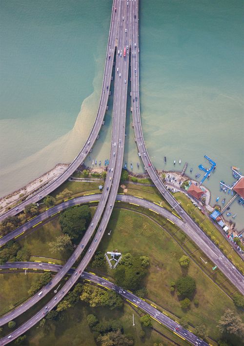 Free Aerial shot capturing an intricate highway and bridge network above a vibrant waterway, surrounded by green spaces. Stock Photo