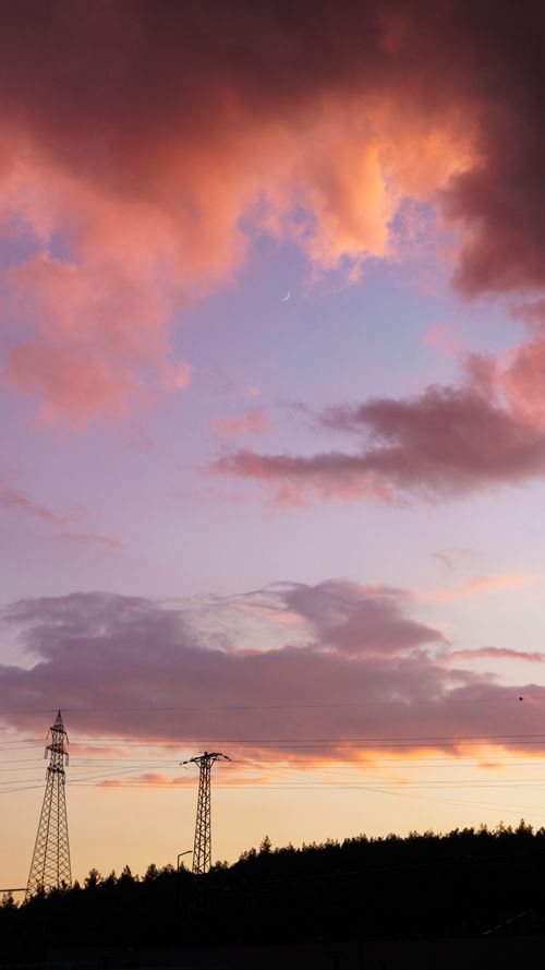 Free A vibrant sunset sky with dramatic clouds and silhouetted transmission towers. Stock Photo