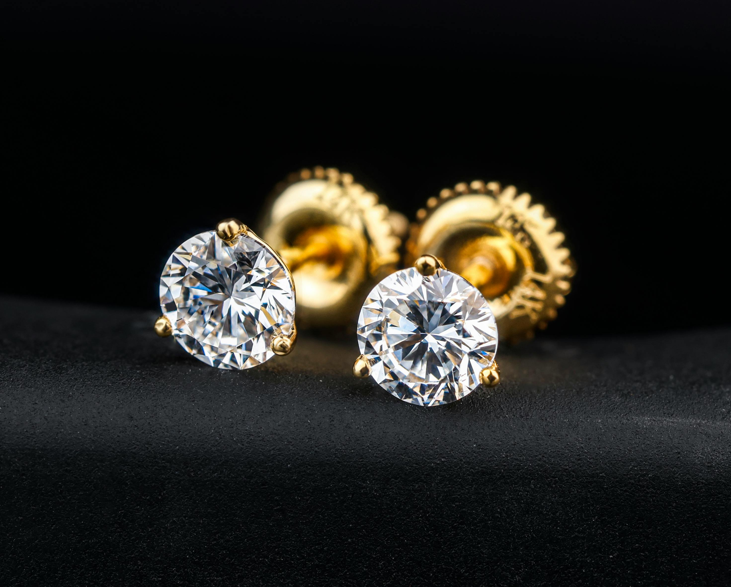 Close-up of small 14K gold diamond stud earrings worn on a woman's ear, minimalist fine jewelry