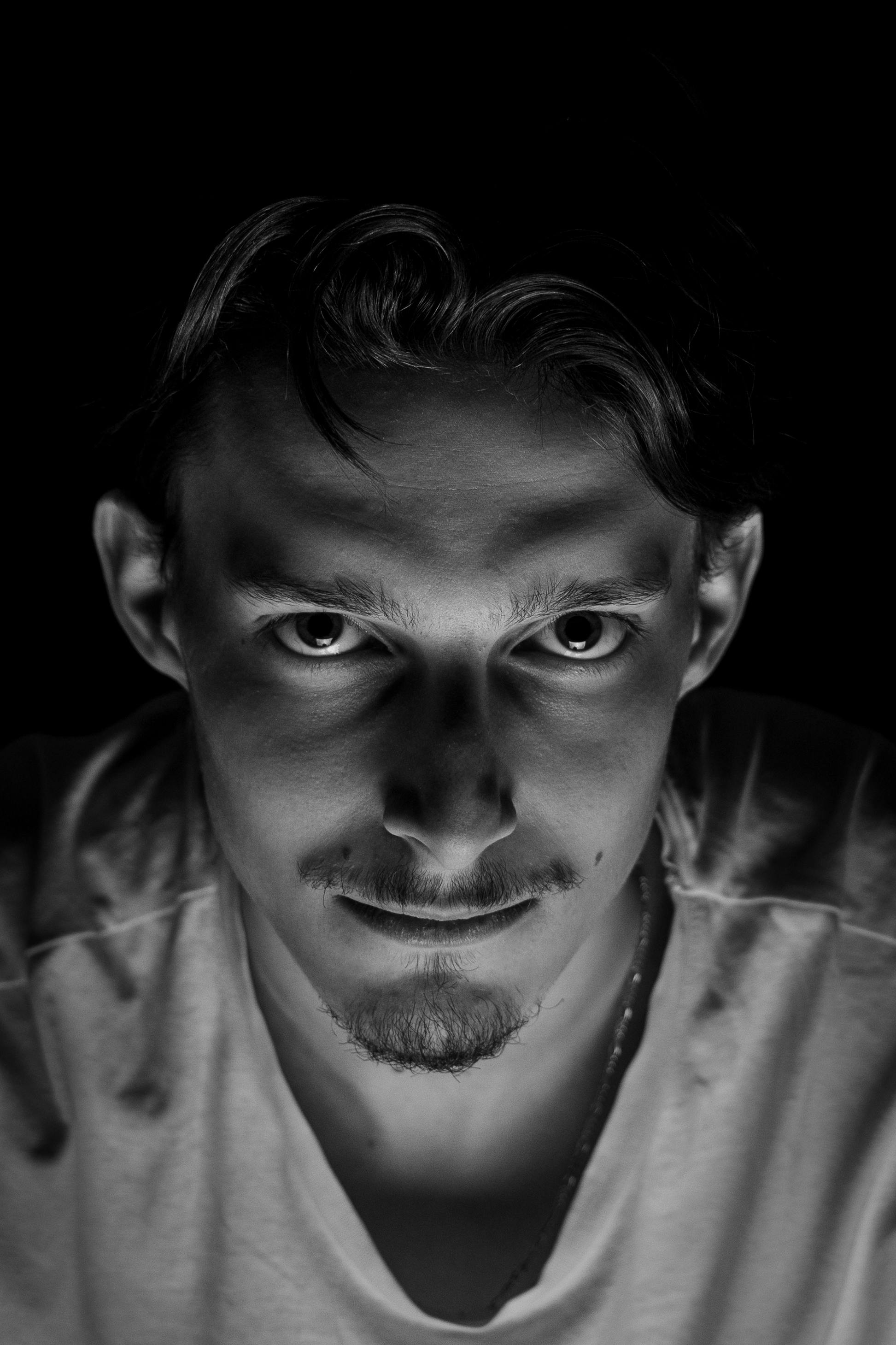 grátis Um retrato dramático em preto e branco de um homem com olhar intenso, capturado sob iluminação de estúdio, evoca mistério. Foto profissional