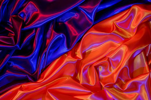 Lustrous red and blue satin fabric with a vibrant sheen creating abstract patterns and folds.