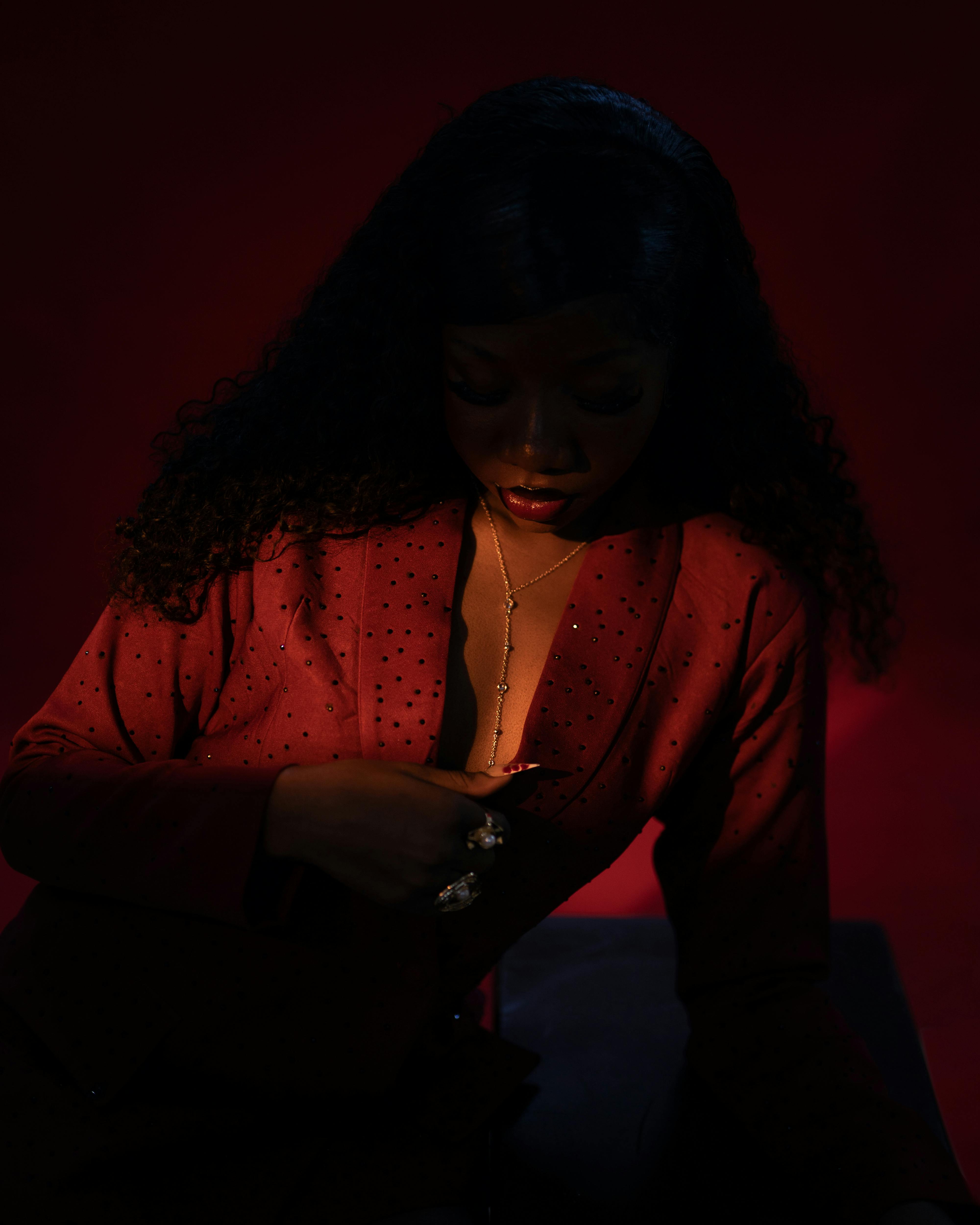Безкоштовне Стильна жінка в червоному костюмі демонструє елегантні прикраси на темно-червоному фоні. стокове фото