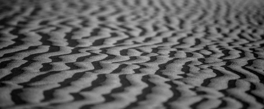 Monochrome close-up of wind-sculpted desert sand patterns in soft focus.
