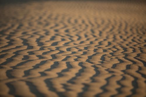 Free Textured sand dunes with intricate wave patterns captured at sunset, creating shadows and depth. Stock Photo