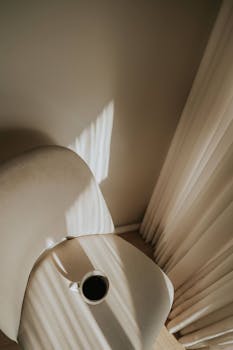 Warm sunlight casting shadows over a modern chair and coffee cup, creating a serene minimalist setting.