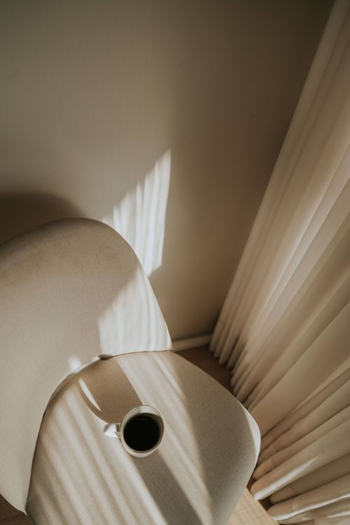 Free Warm sunlight casting shadows over a modern chair and coffee cup, creating a serene minimalist setting. Stock Photo