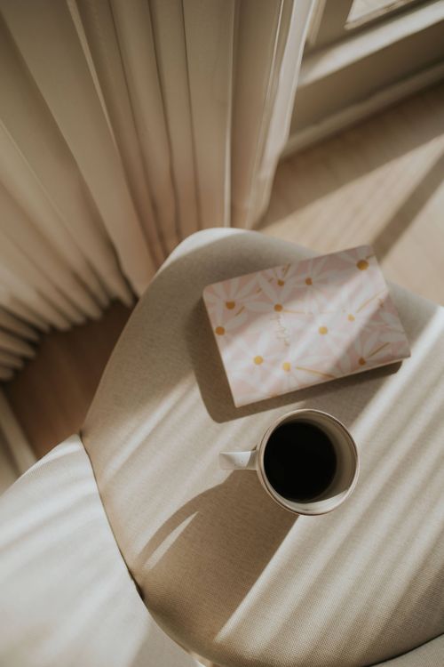 Free Sunlit chair with coffee cup and book, creating a serene reading atmosphere. Stock Photo
