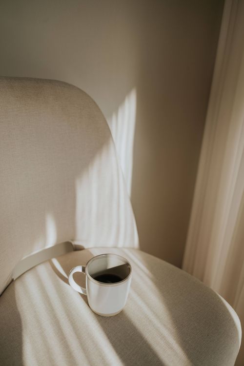 Free A white coffee cup on a chair with sunlit shadows creating a minimalist composition. Stock Photo