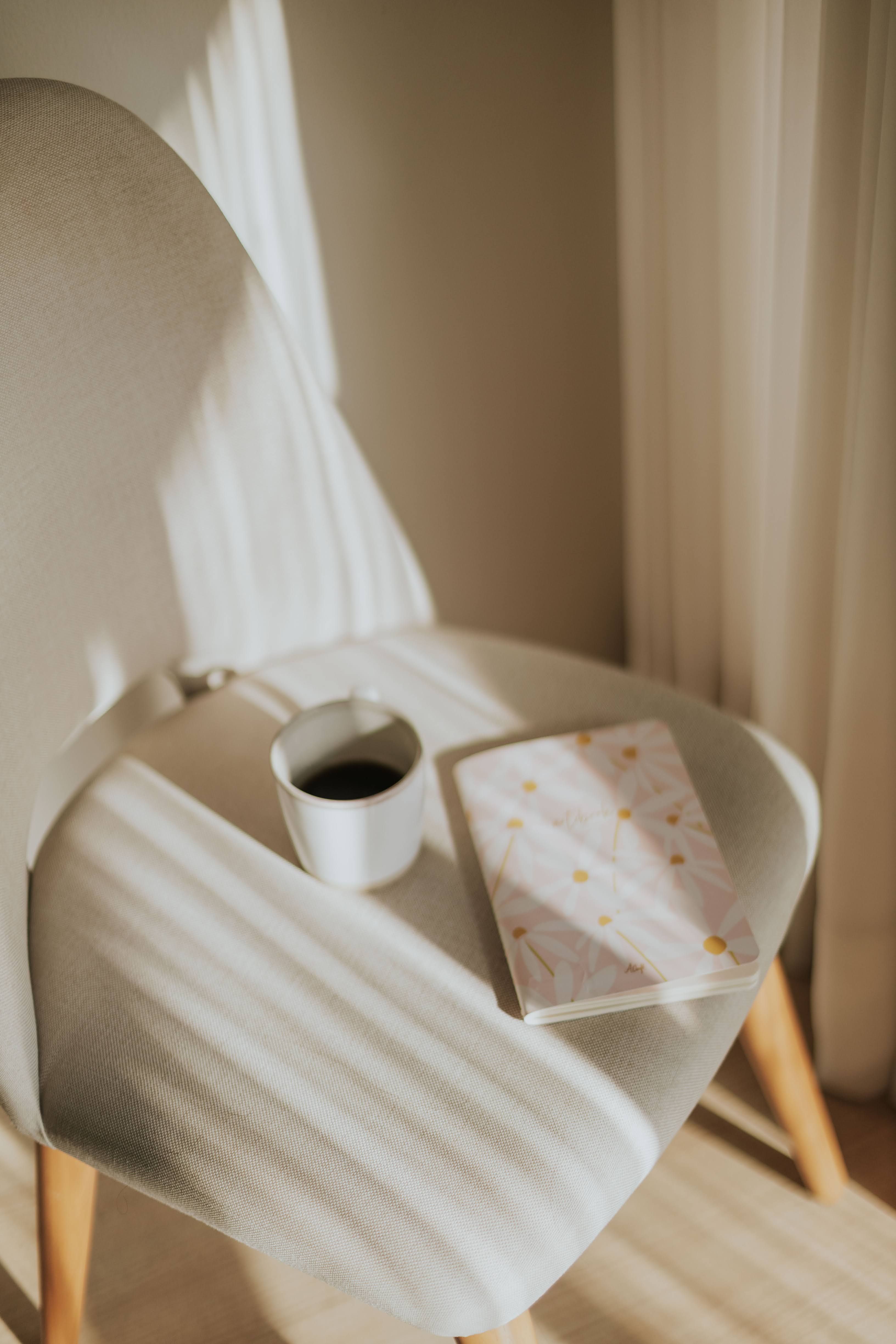 Minimalist beige chair with coffee and notebook in warm morning sunlight.