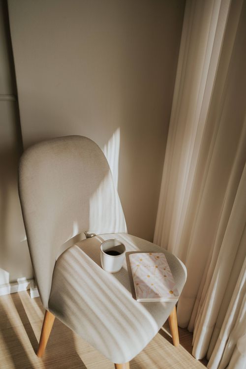 Free A peaceful morning scene with coffee and a journal on a chair by the window. Stock Photo