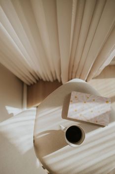 Elegant table setup with coffee and book bathed in gentle morning sunlight through curtains.