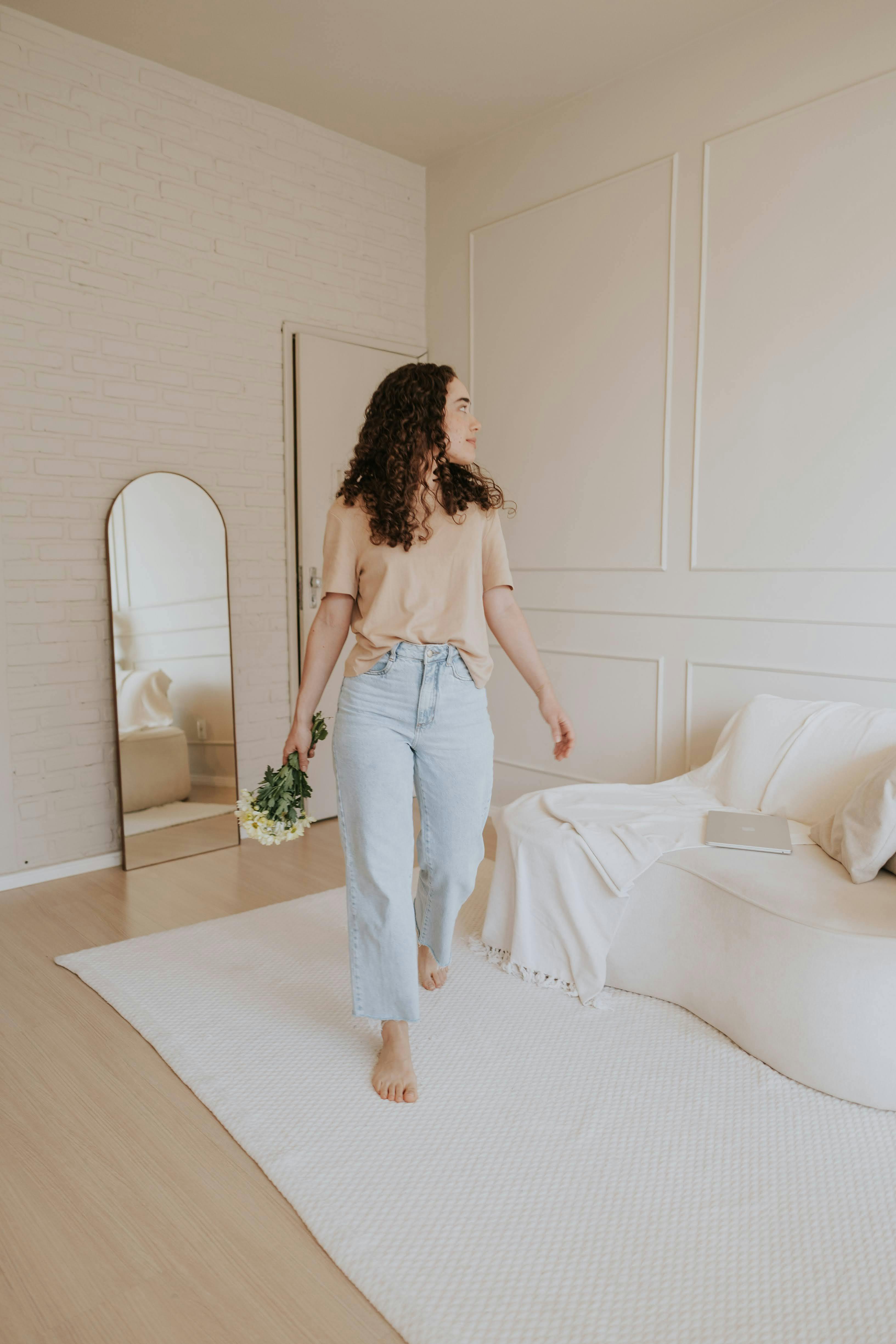 Woman in a cozy, minimalist room with flowers, exuding warmth and simplicity.