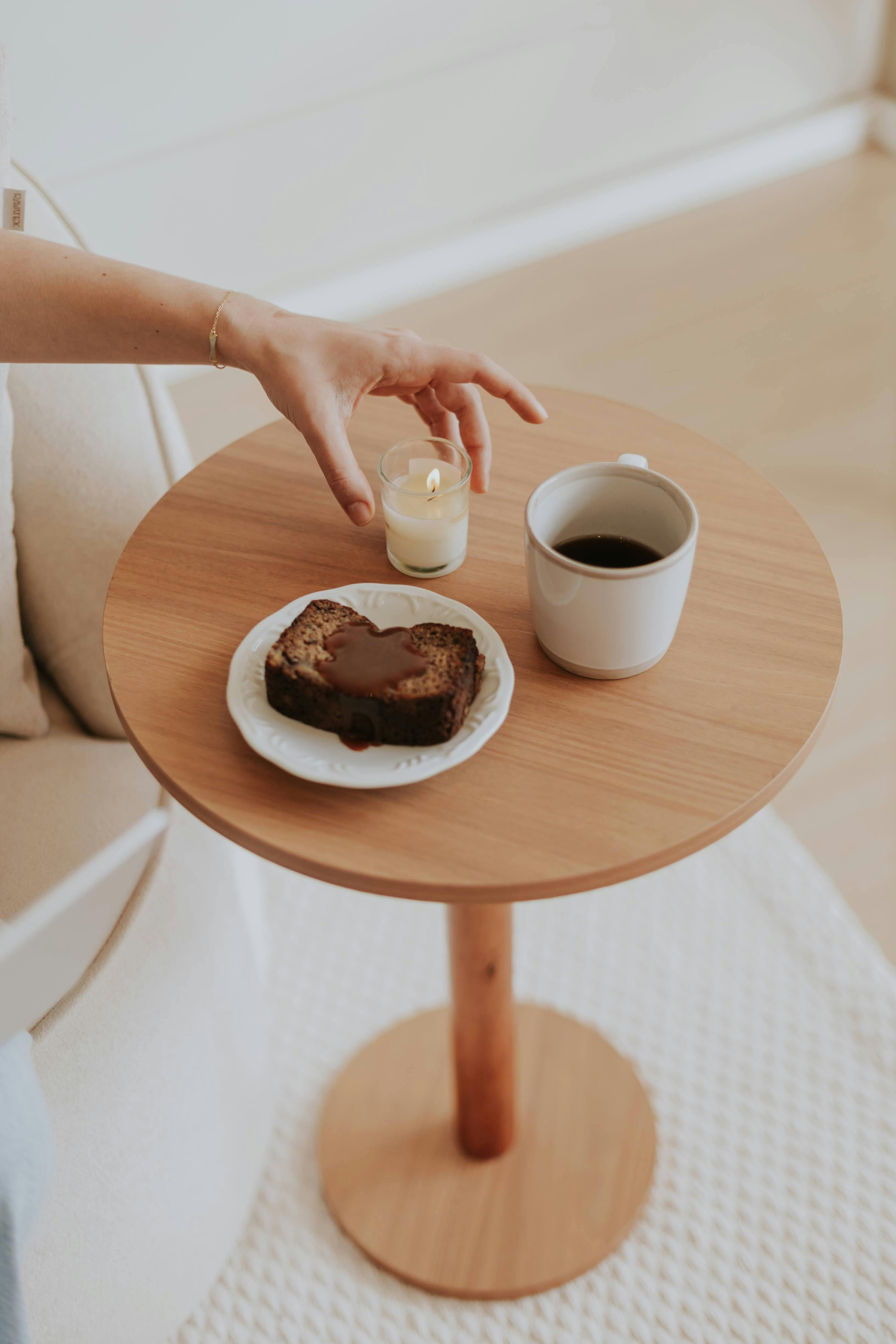 A cozy indoor setup with coffee, cake, and a candle on a wooden table.