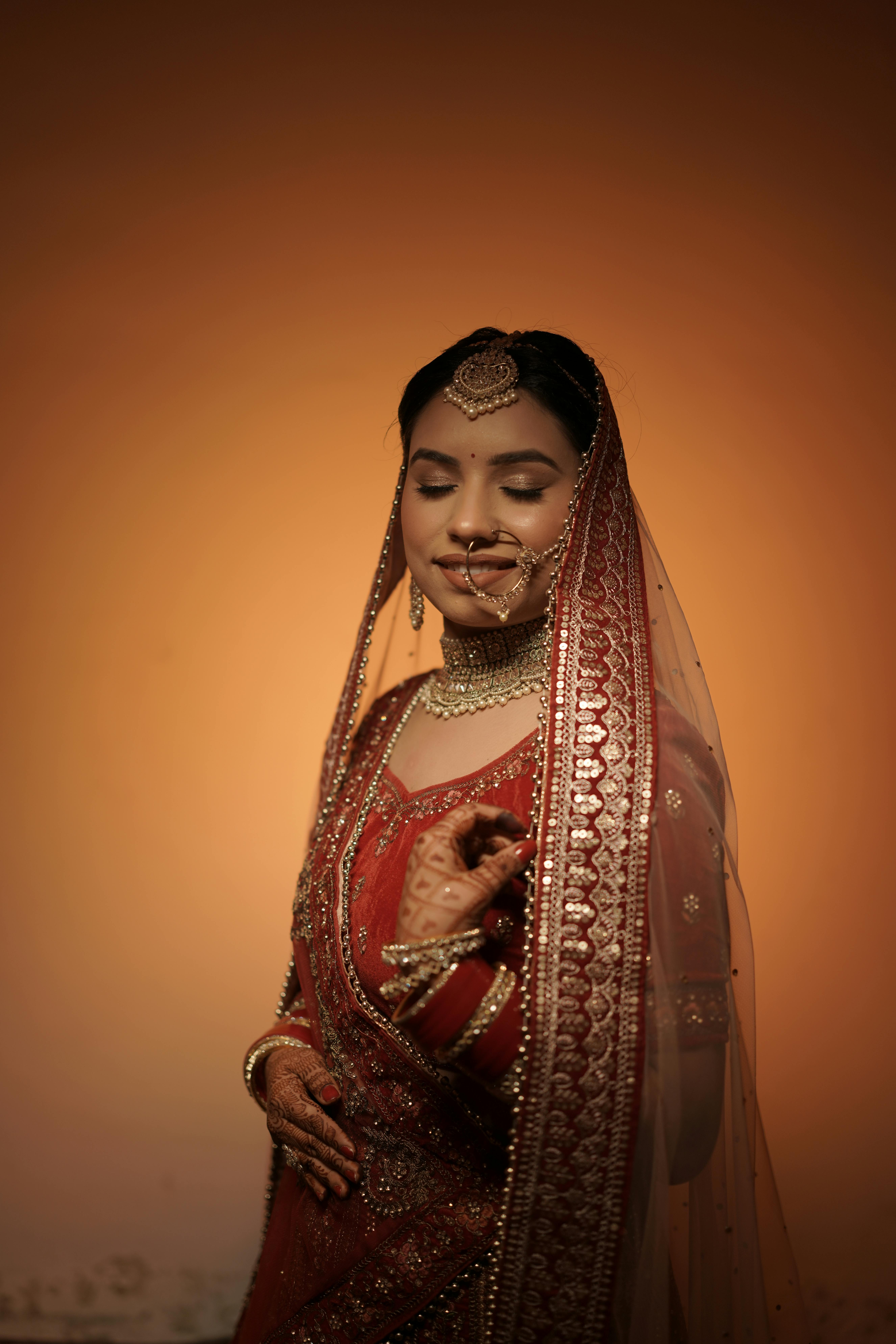 South Asian bride in red bridal lehenga with intricate henna designs, looking serene.