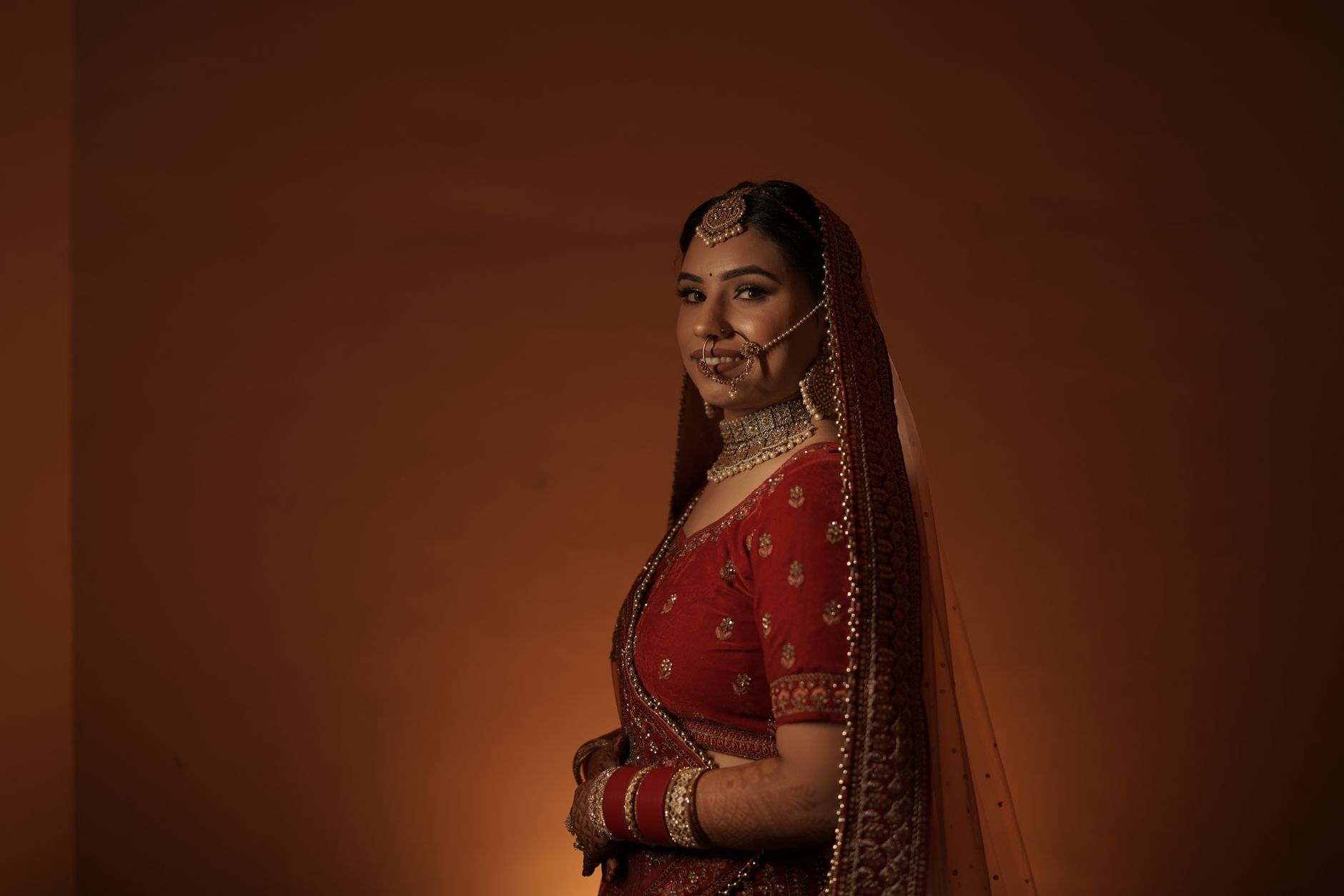 A beautiful Indian bride in traditional red lehenga and jewelry, posing gracefully.