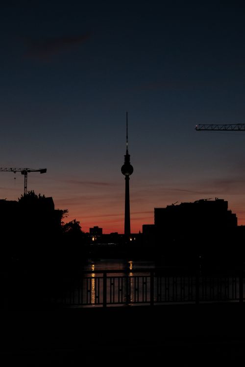 Free Silhouette of Berlin's TV Tower against a twilight sky with cranes and cityscape. Stock Photo