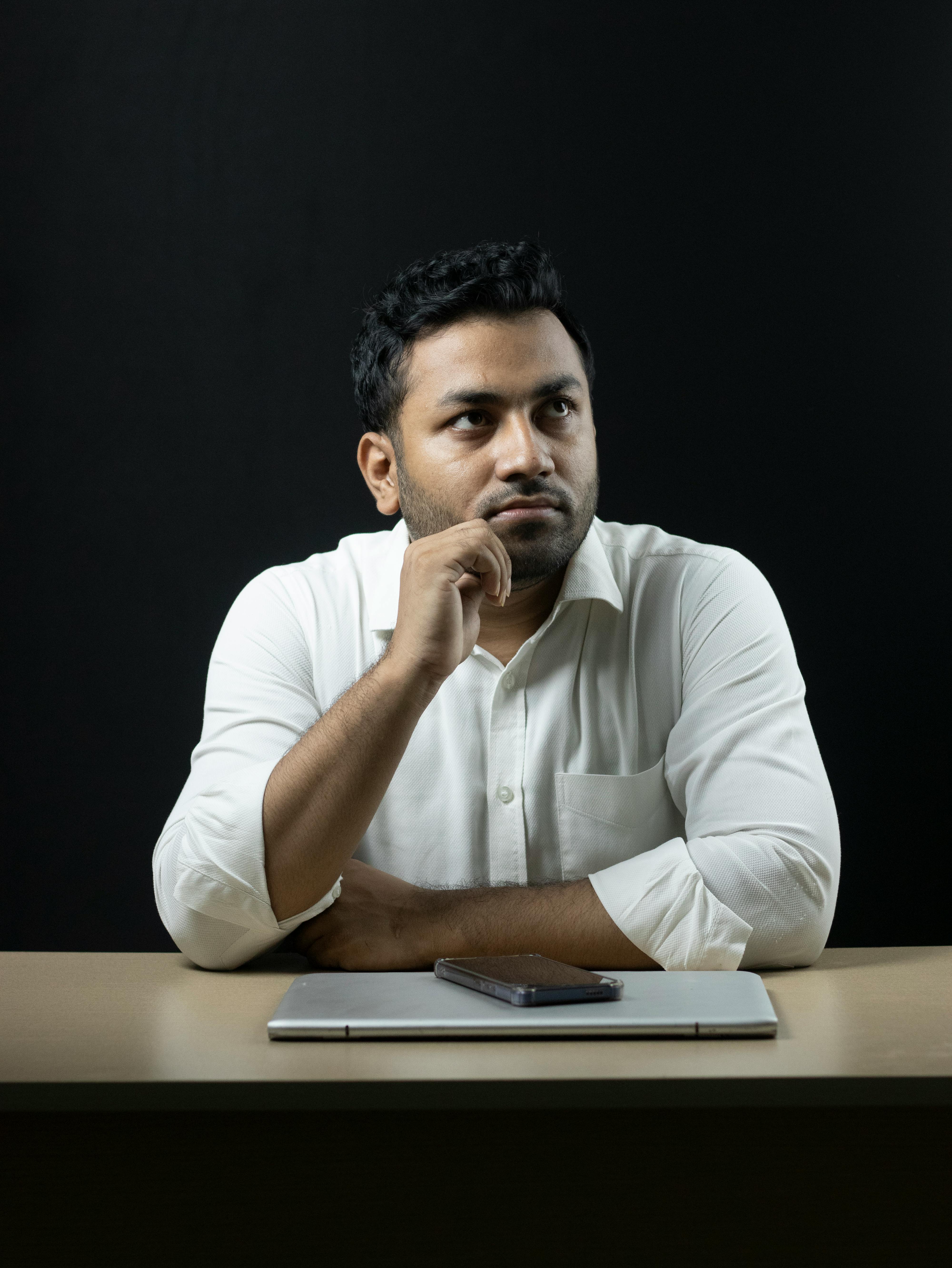 Thoughtful businessman seated at a desk with a laptop and phone, deep in reflection.