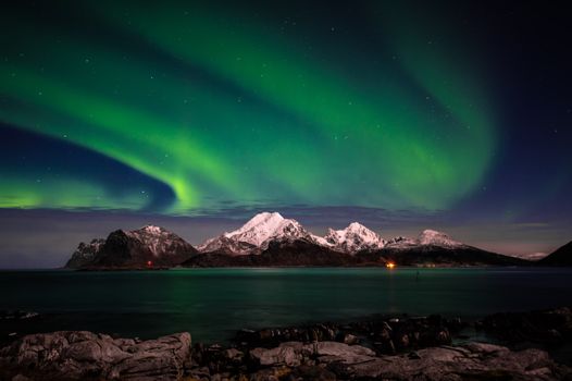Stunning view of the Northern Lights over snowy mountains and sea in Norway.