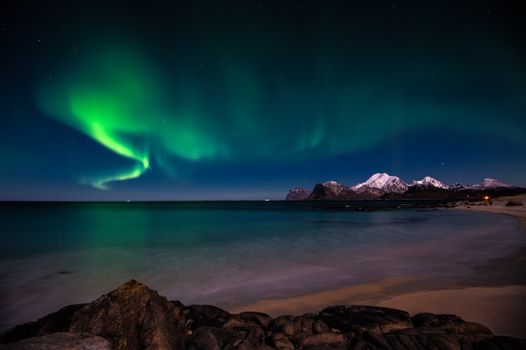 Breathtaking view of Aurora Borealis illuminating a serene beach with snow-capped mountains.