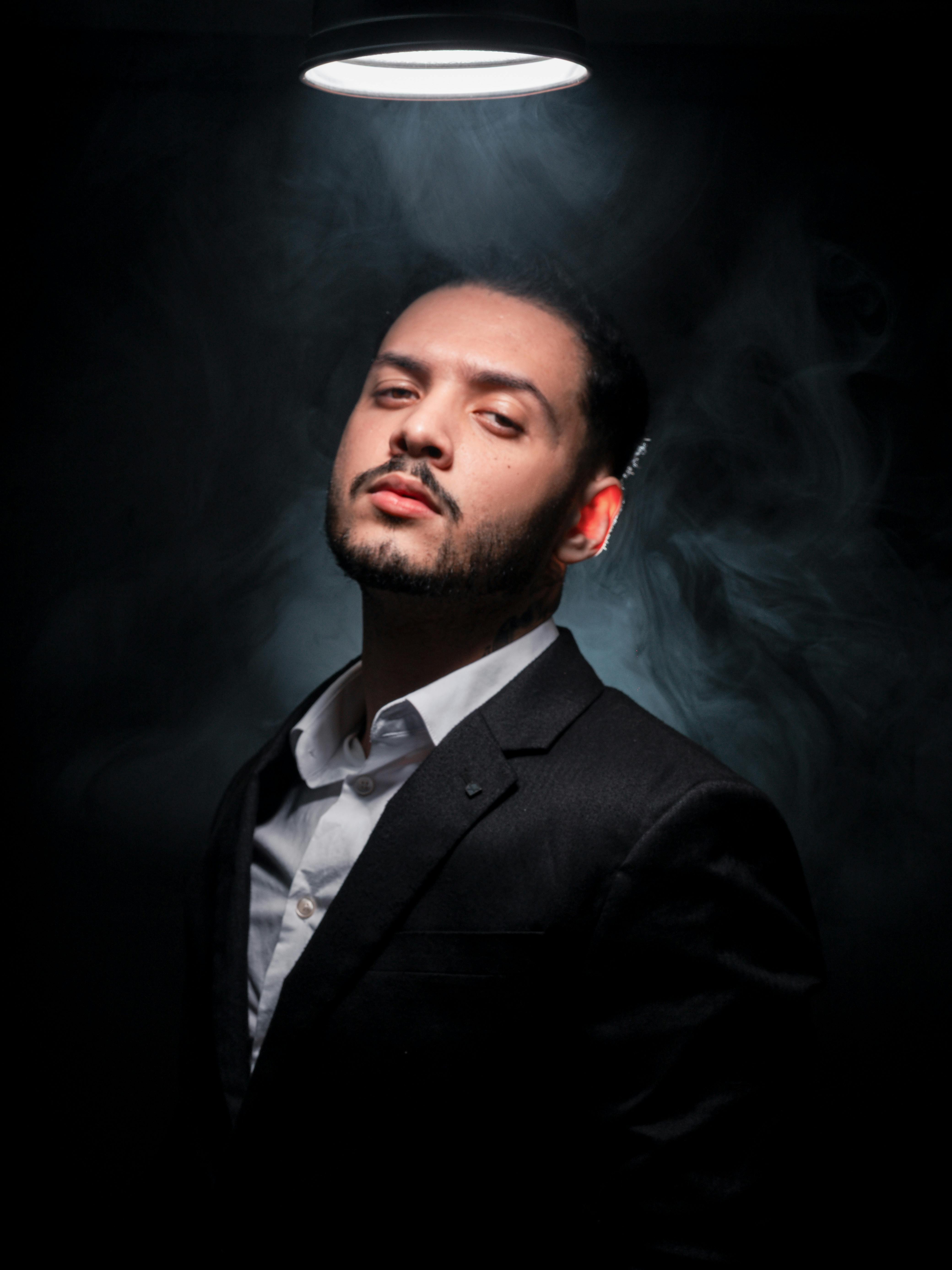 Moody portrait of a confident man in a black suit with dramatic lighting and smoke effect.