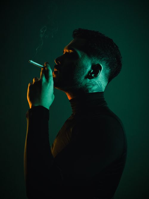 Free Artistic portrait of a man smoking, captured in striking low-light with vivid contrast. Stock Photo