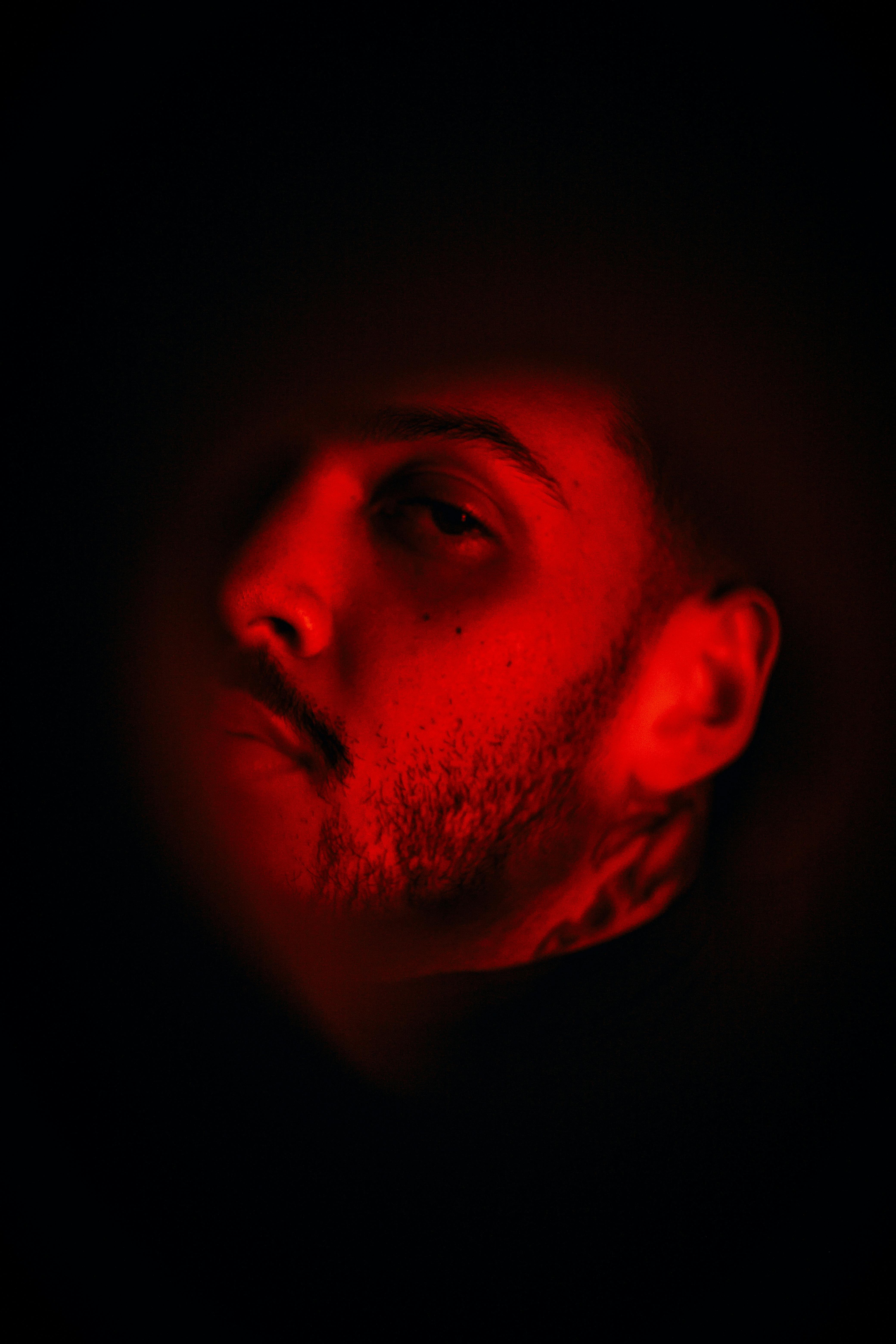 grátis Retrato intenso de um homem sob uma iluminação vermelha dramática, criando uma atmosfera misteriosa. Foto profissional