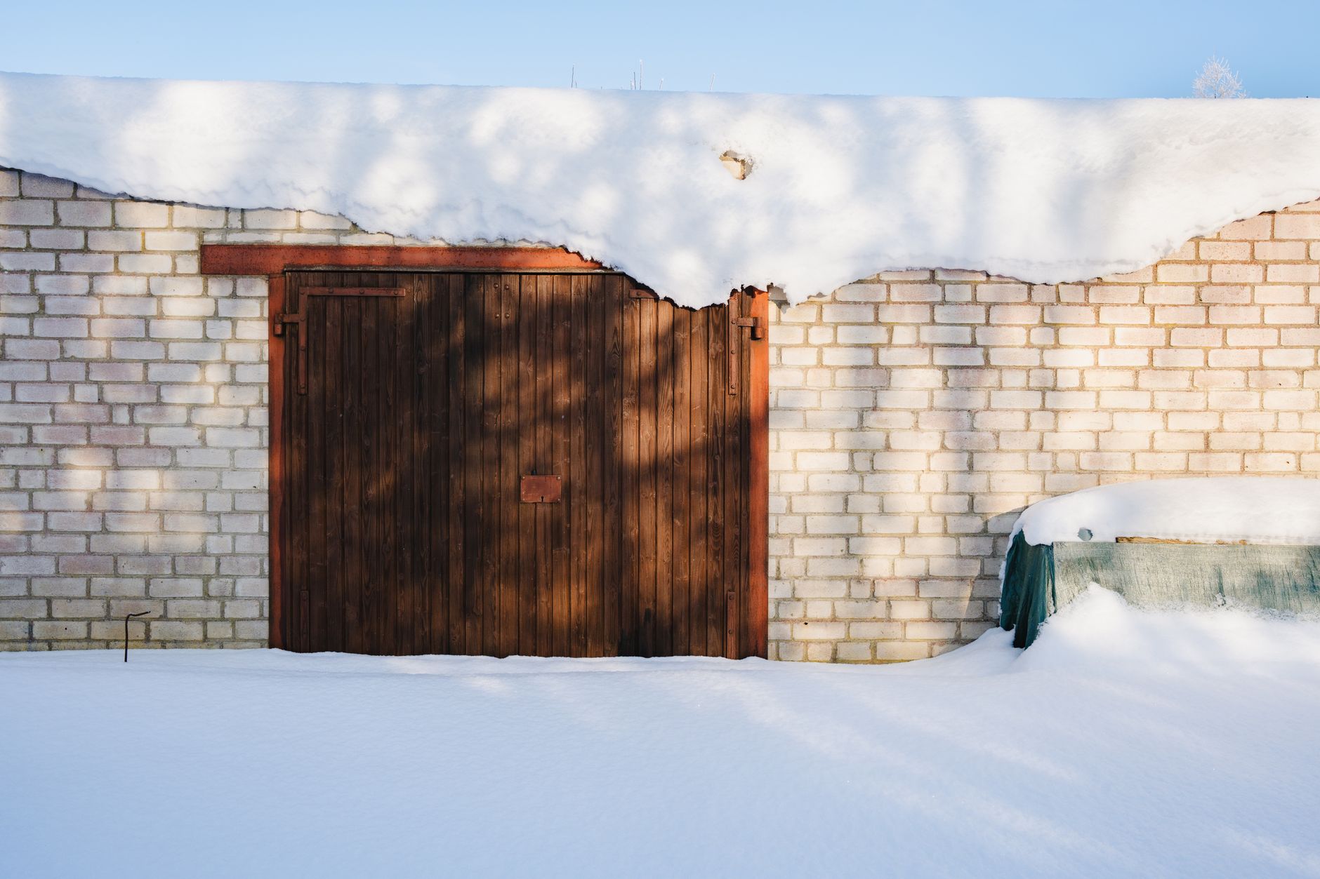 A snow-covered brick garage door under a blue sky with winter shadows.