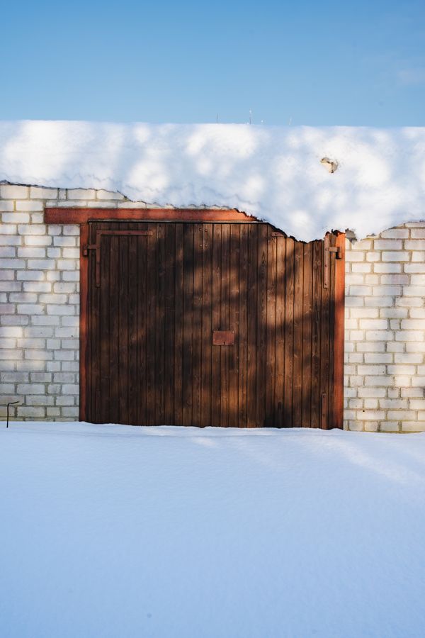Uma porta de garagem de madeira emoldurada por paredes de tijolos sob um céu azul claro com neve fresca.