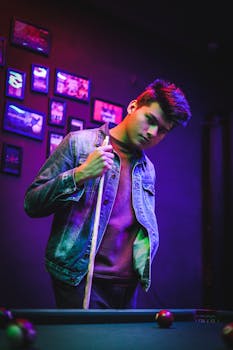 一位时尚的年轻人在夜总会色彩缤纷的灯光下，自信地拿着台球杆摆出姿势