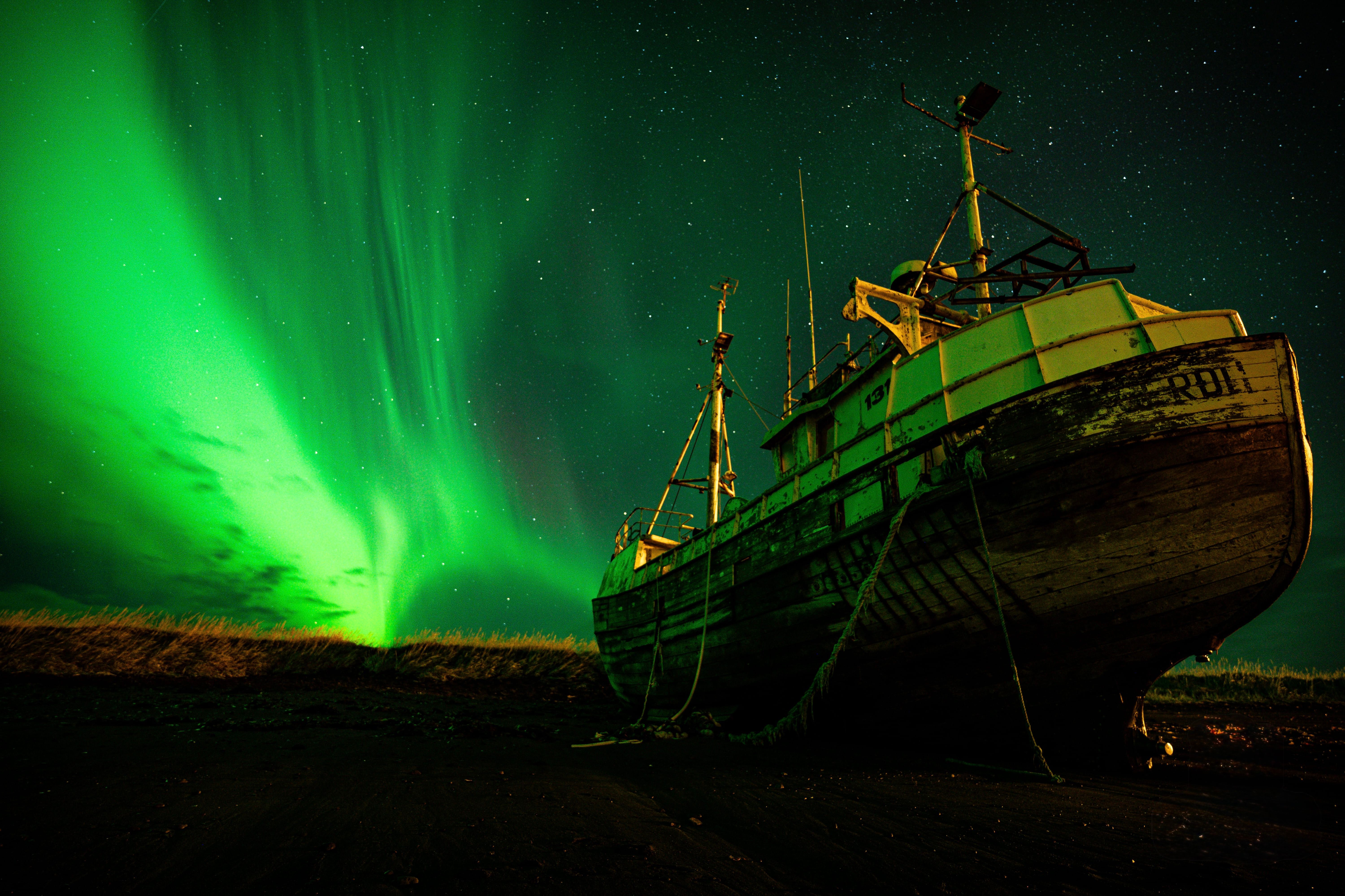Rustic boat under vibrant green aurora borealis in a starry Icelandic night sky.