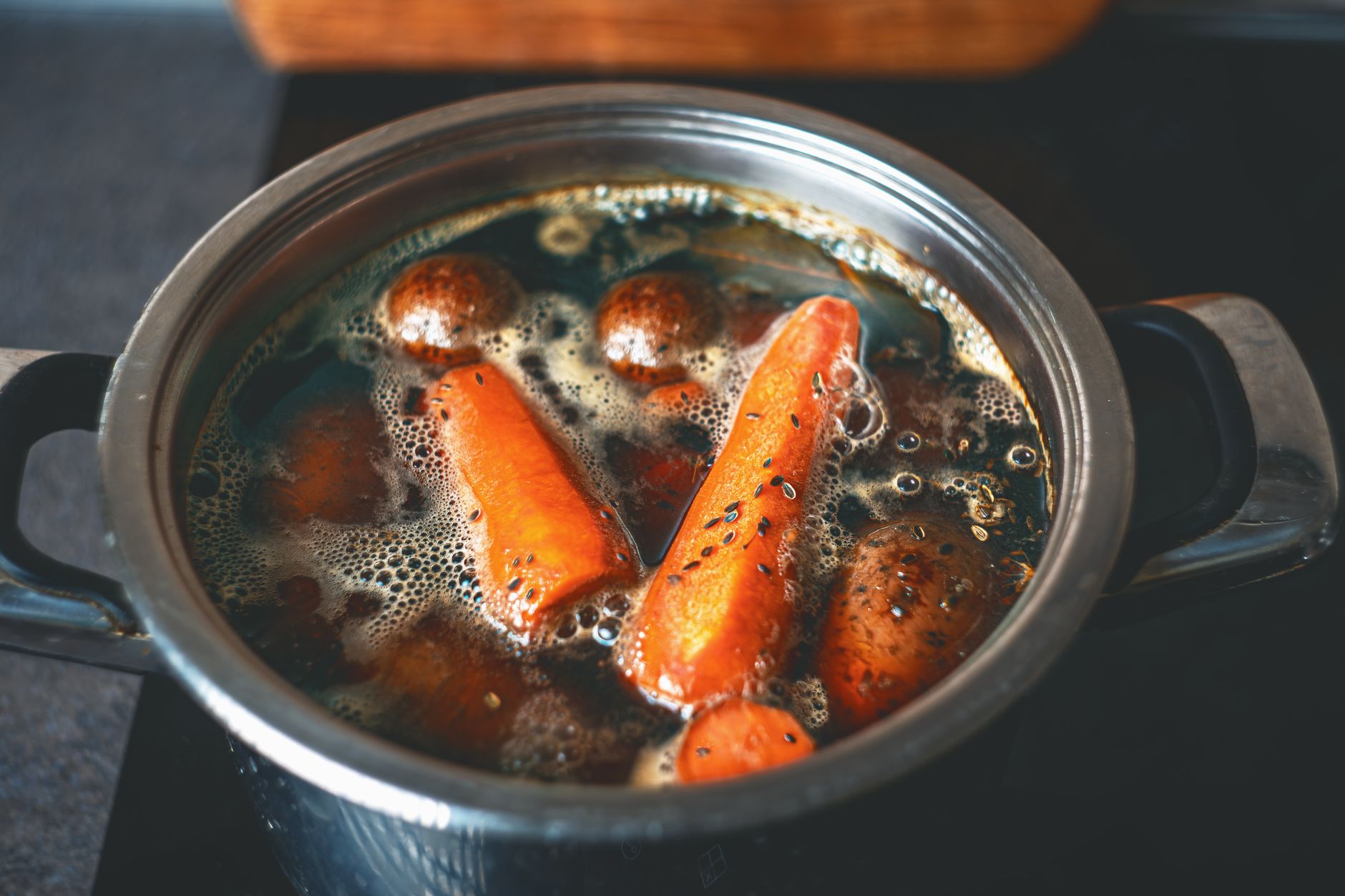 A close-up of carrots and potatoes boiling in a metal pot on a stove.