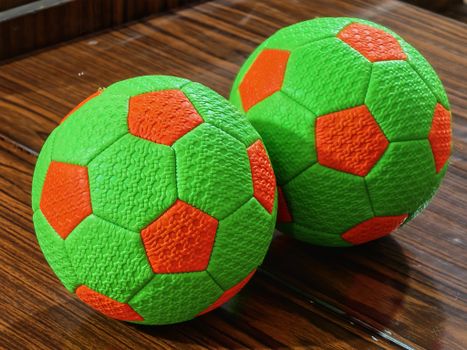 Close-up of two vibrant green and orange soccer balls resting on a wooden floor indoors.