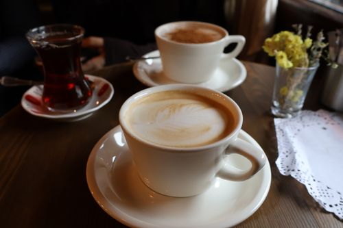Free Inviting scene with two lattes and a tea glass on a wooden table, perfect for coffee shop vibes. Stock Photo