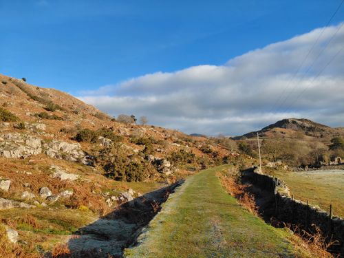 Free A tranquil mountain path winding through rocky hills under a blue sky with clouds. Stock Photo