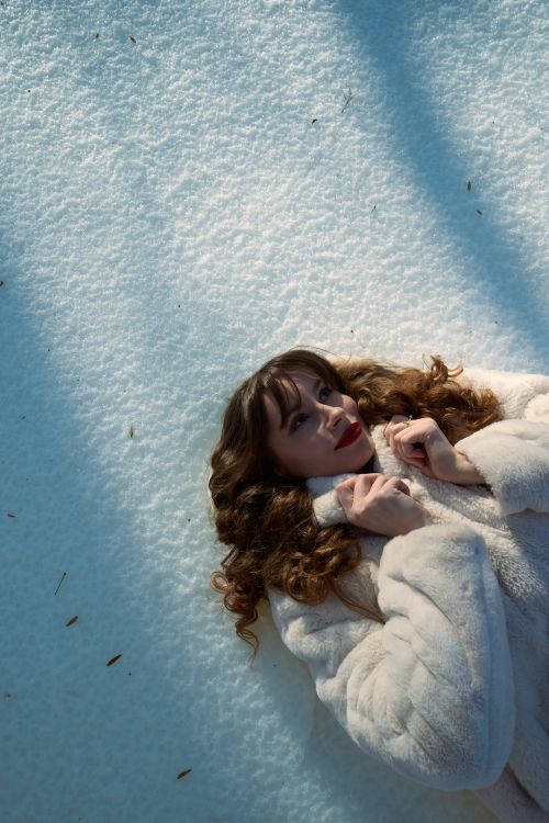 Free Elegant woman in a white fur coat lying on snow, enjoying a winter day. Stock Photo