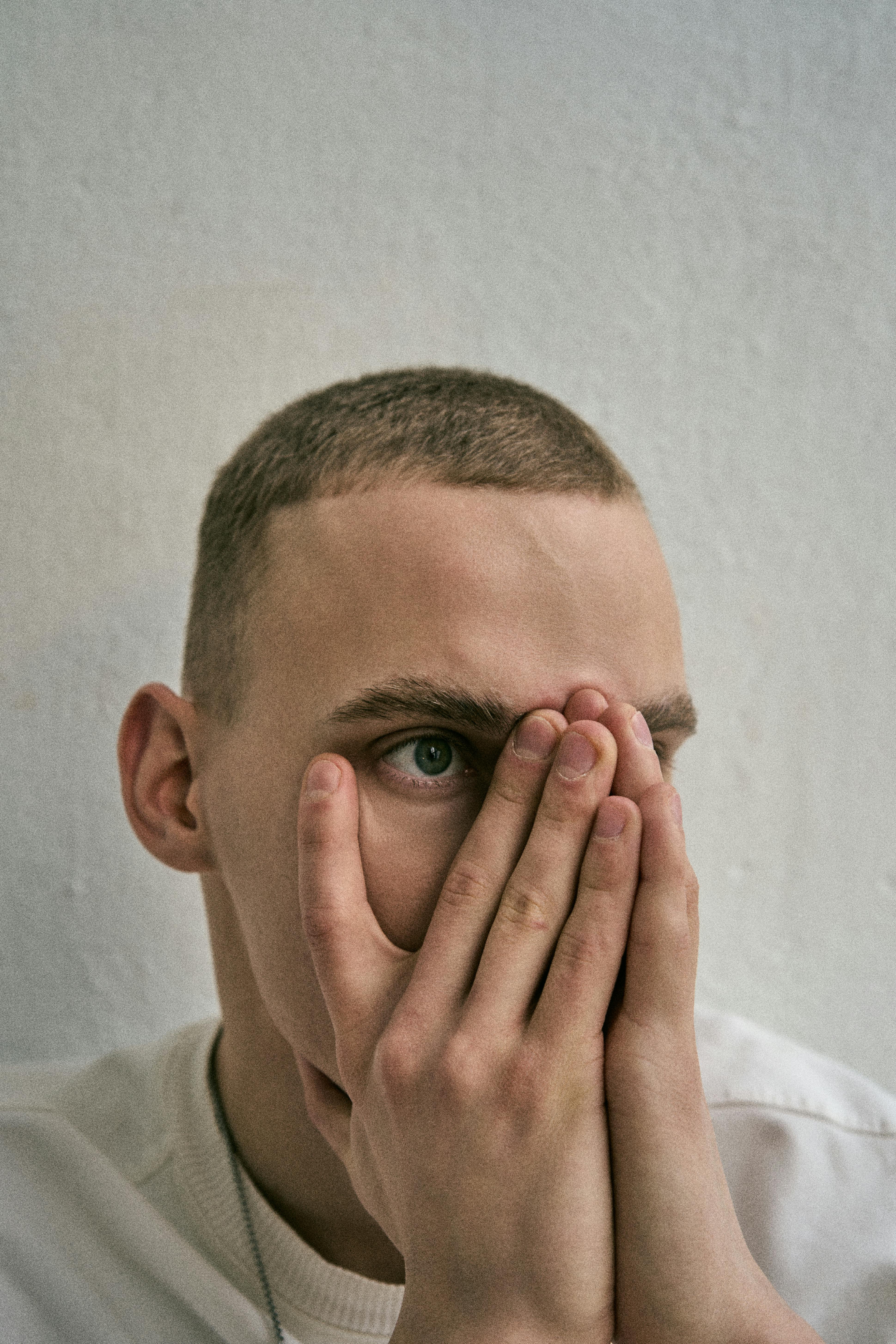 Close-up portrait of a young man covering his face, showcasing a pensive mood.