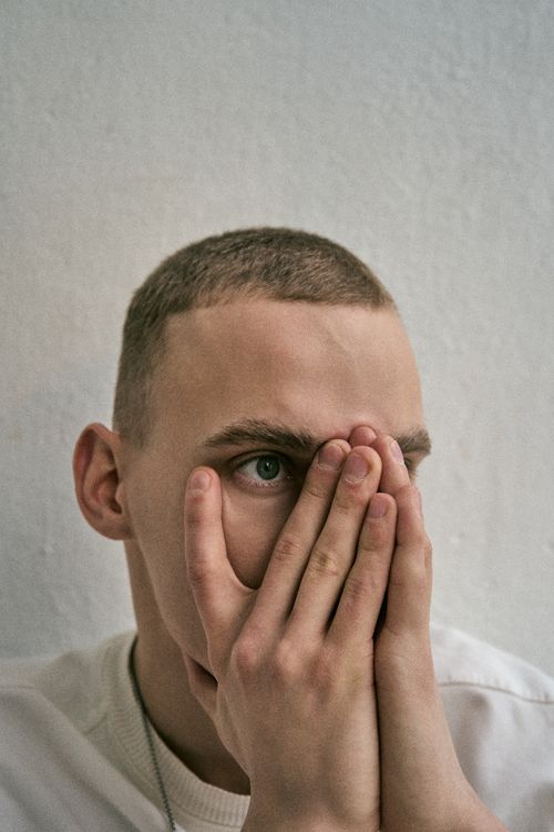 Free Close-up portrait of a young man covering his face, showcasing a pensive mood. Stock Photo