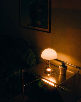 Warmly lit minimalist interior with lamp, metal table, and houseplant.