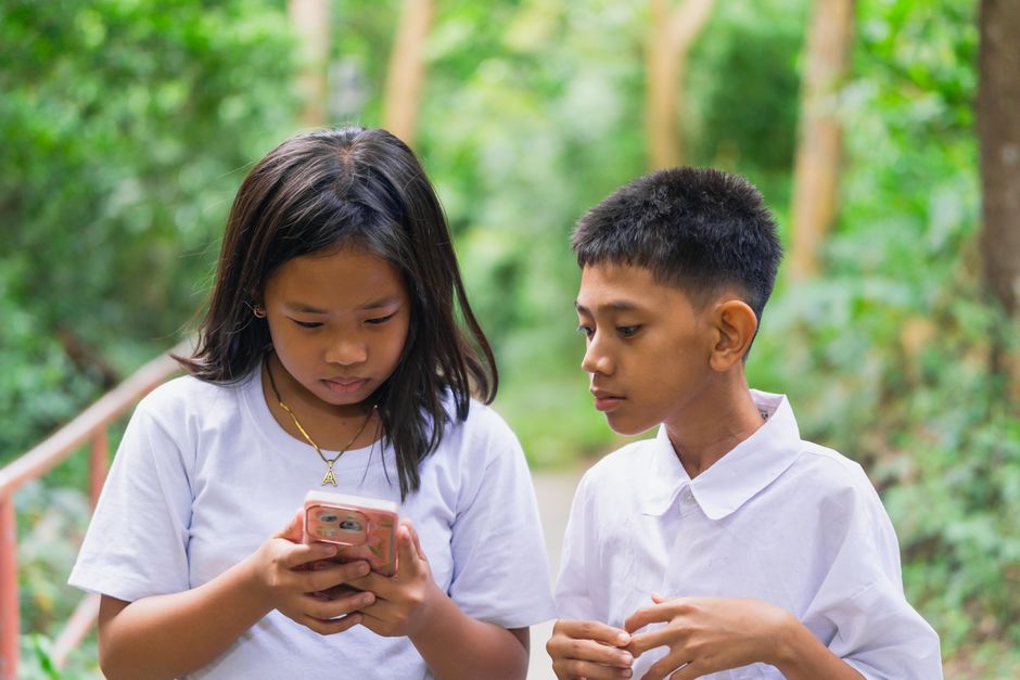 Photo by Nothing Ahead on Pexels Two children engaging with a smartphone in a lush outdoor setting.