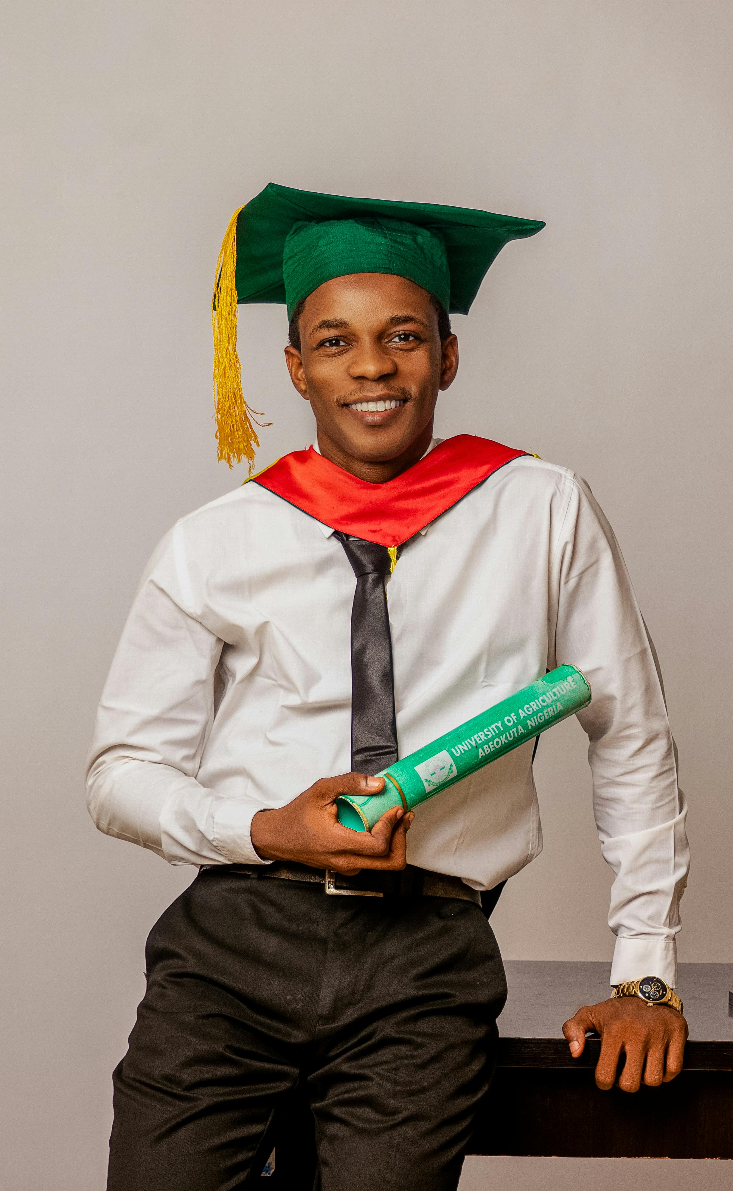 Confident young graduate in cap and gown holding diploma indoors.