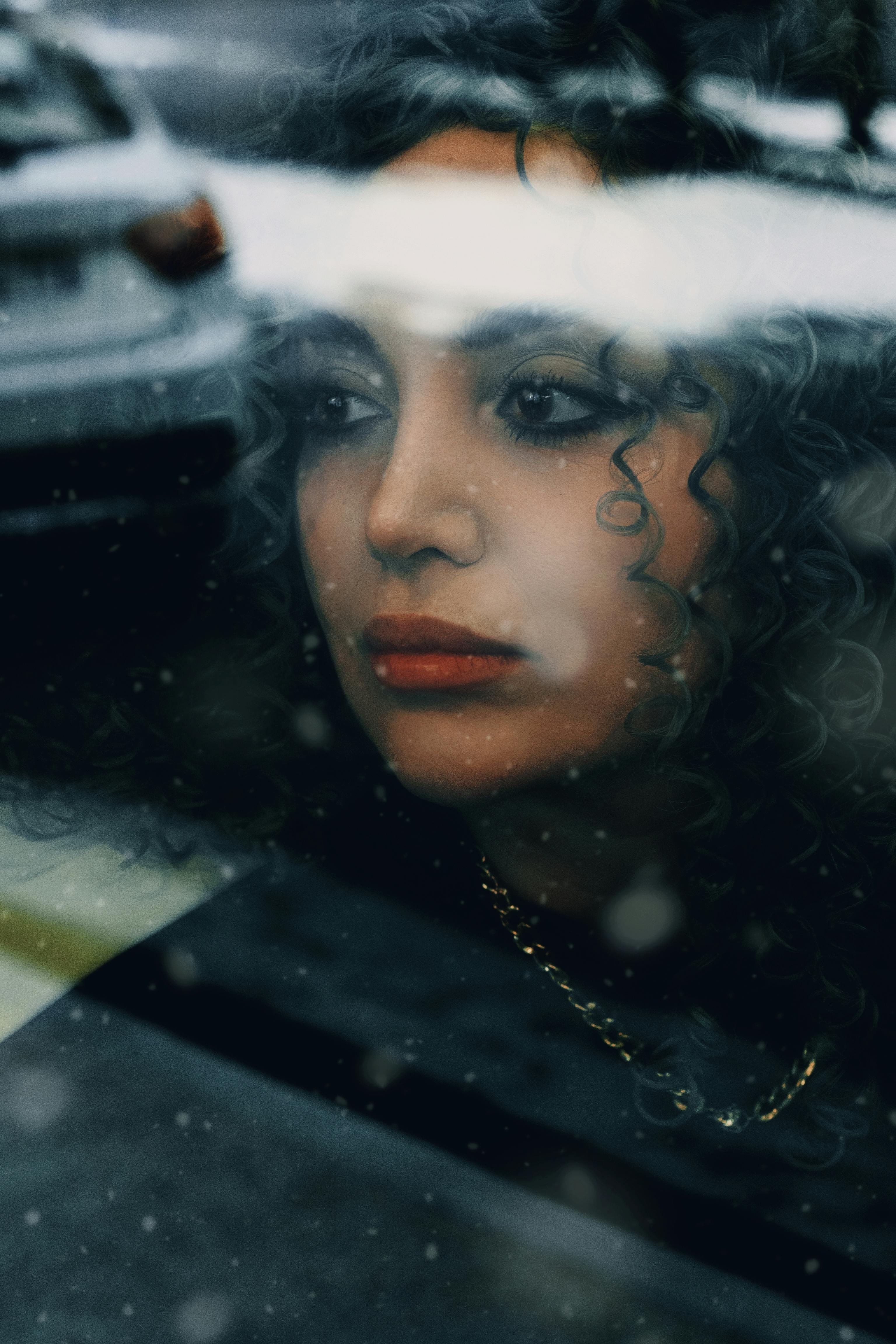 Gratis Ritratto malinconico di una donna che guarda attraverso una finestra punteggiata di pioggia, evocando introspezione. Foto a disposizione